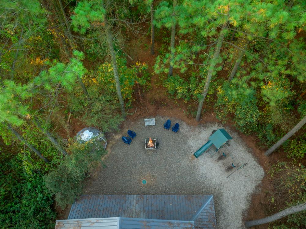 Aerial views showcase the spacious backyard layout, complete with fire pit, play area, and private wooded surroundings.