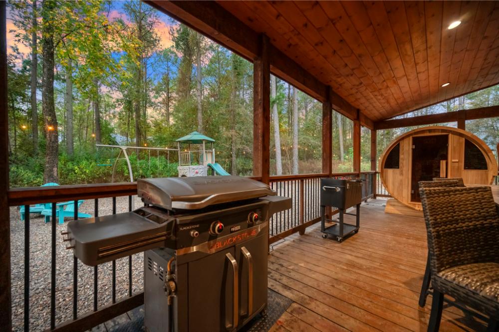 The covered deck features a Blackstone griddle, sauna, and play space, making it ideal for entertaining day or night.